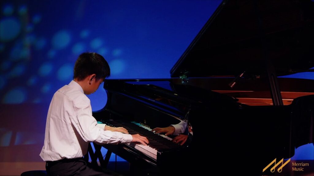 Student pianist performing on a grand piano under blue stage light