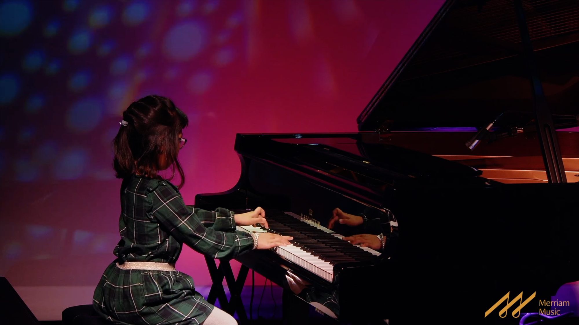 Young pianist performing on a grand piano under pink stage light